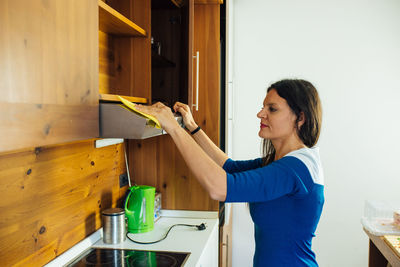 Side view of woman cleaning air duct in kitchen at home