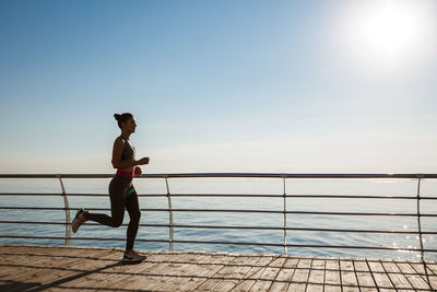 Woman jogging by sea against clear sky