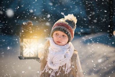 Portrait of smiling young girl standing in snow storm looking at lantern