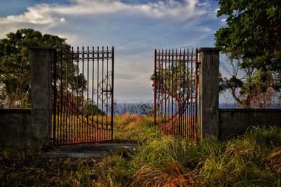 Abandoned gate on field against sky