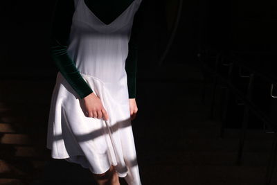 Midsection of woman wearing dress standing in dark room