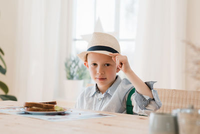 Boy sat eating his breakfast dressed smartly with a hat