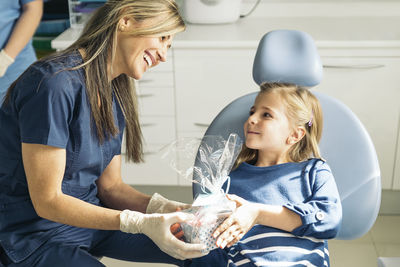 Smiling female dentist giving gift to girl at clinic