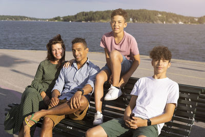 Portrait of smiling family sitting together on bench near sea