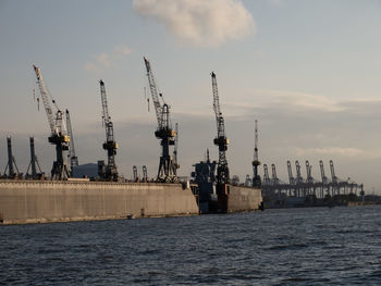 Cranes at commercial dock against sky