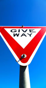 Low angle view of road sign against clear blue sky