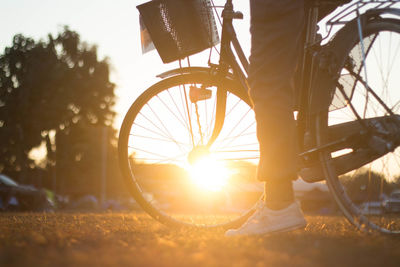 Low section of man with bicycle against sky during sunset