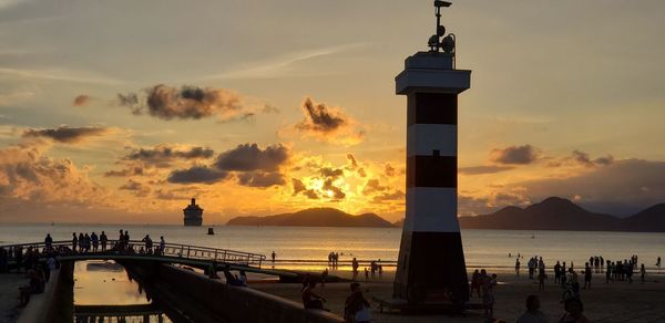 Lighthouse by sea against sky during sunset