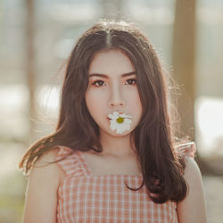 Portrait of beautiful young woman with flower in mouth