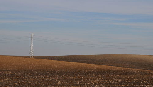 Electricity pylon on field against sky