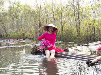 Full length portrait of woman sitting by plants against trees