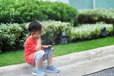 Thoughtful boy with container sitting on footpath