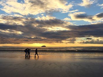 Silhouette people walking on beach against sky during sunset