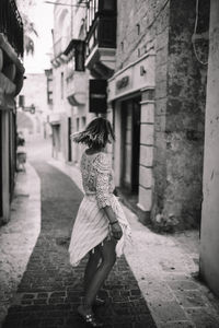 Rear view of woman walking on footpath amidst buildings