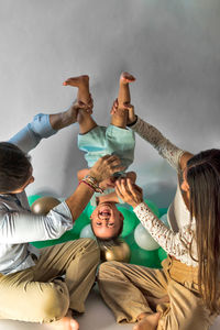 Parents playing with small baby while holding legs and tickling in studio decorated with balloons for celebrating birthday together