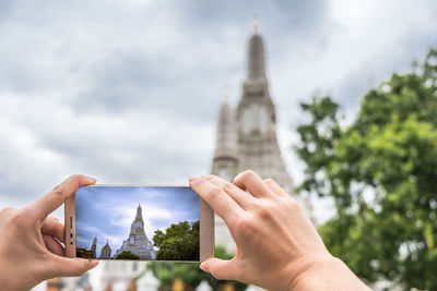 Cropped image of hand holding smart phone against sky