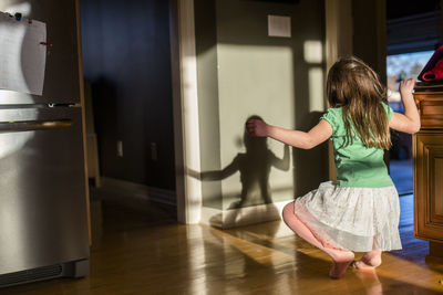 A little girl dances with her shadow in a sunlit kitchen