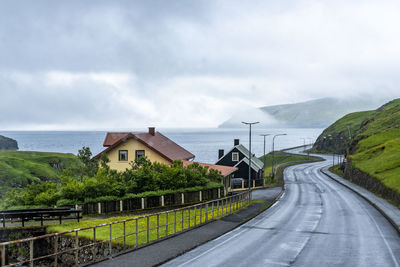 Road by sea and buildings against sky