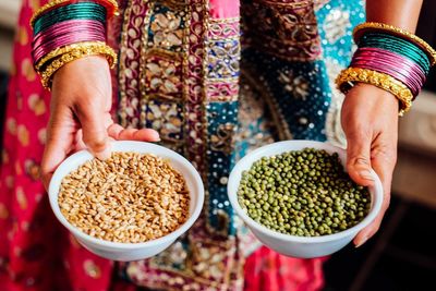 Midsection of woman in bangles holding wheat and mung bean bowls