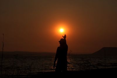 Silhouette man reaching sun at beach