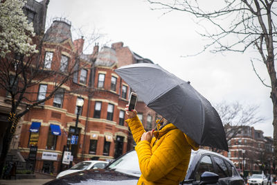 Side view of woman with umbrella using mobile phone in city