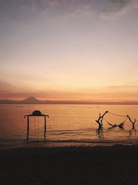 Silhouette parasols on beach against sky during sunset