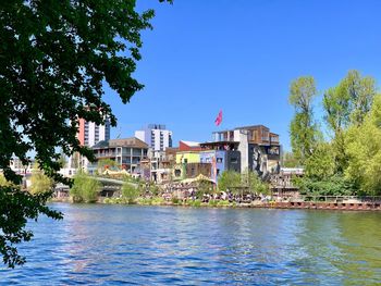 View of buildings by river against blue sky