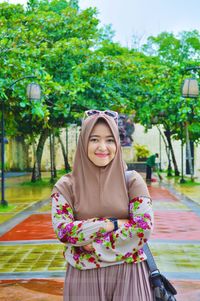 Portrait of smiling young woman standing against trees