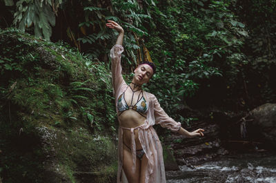 Woman with arms raised standing against tree in forest