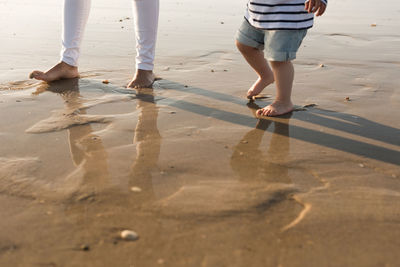Low section of mother and son walking at beach