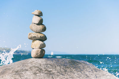 Stacked rocks by sea against clear sky