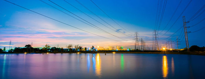 Electricity pylon by river against sky during dusk