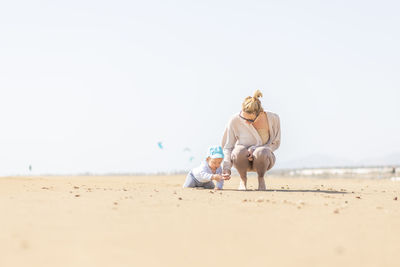 Rear view of woman sitting on sand at beach against clear sky