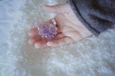 Close-up of cropped hand holding gemstone on bed at home