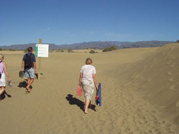 People walking on sand dune in desert against clear sky