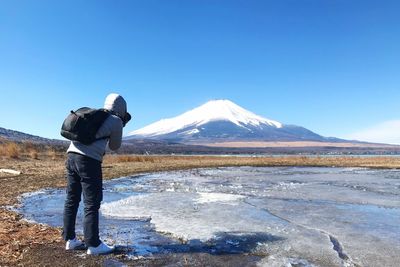 Rear view of woman standing on snowcapped mountain against clear sky