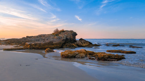 Rocks on beach against sky during sunset