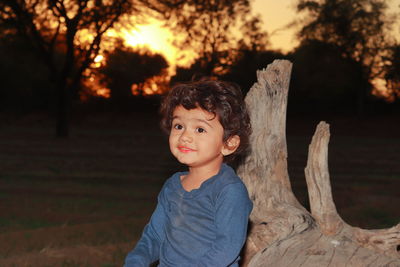 A beautiful and small indian male child sitting on the wood and playing at sunset