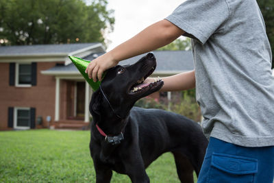 Midsection of boy wearing party hat to dog at yard
