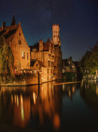 Illuminated buildings by river against sky at night