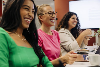 Happy businesswoman sitting with colleagues during meeting at work place