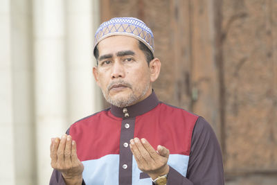 Portrait of mature man praying while sitting at mosque