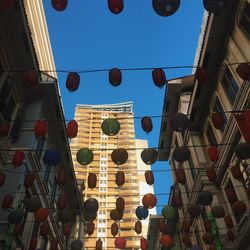 Low angle view of lanterns hanging amidst buildings against clear blue sky
