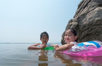 Portrait of siblings swimming in sea against clear sky