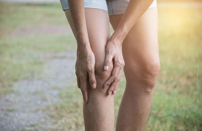 Close-up of person holding knee while standing on land