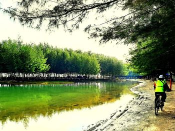 People riding bicycle by lake against sky