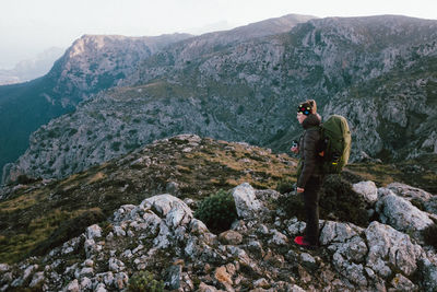 Woman holding drink looking away while standing against mountains