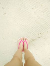Low section of woman in pink slipper on sand at beach