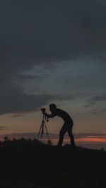 Silhouette man photographing on land against sky during sunset