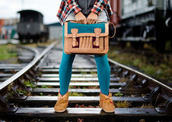 Low section of man holding bag while standing on railroad track